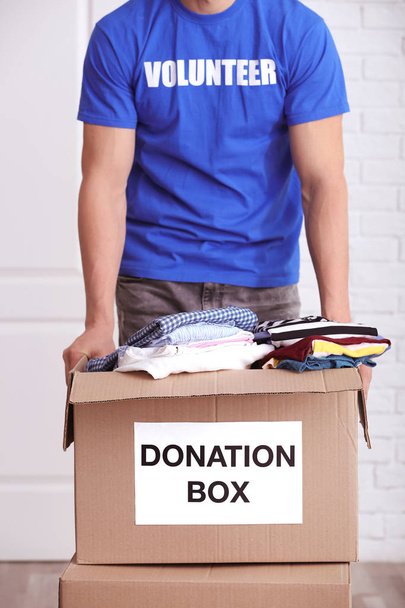 Male volunteer holding donation box with clothes indoors - Φωτογραφία, εικόνα