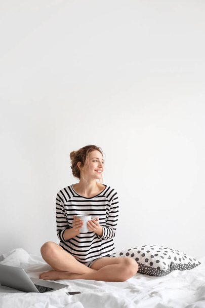 Female blogger with laptop and cup of coffee on bed - Photo, image