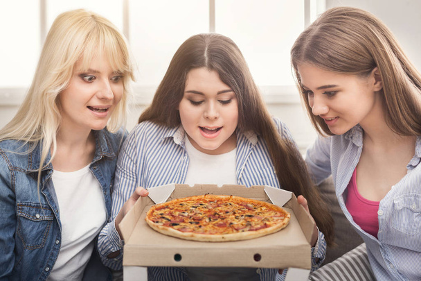 Nahaufnahme von drei Freundinnen, die auf Pizza schauen - Foto, Bild