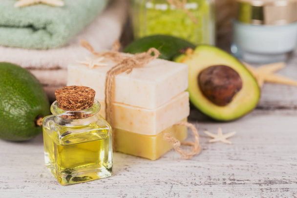 Natural cosmetic oil and natural handmade soap with avocado on white rustic wooden background. Healthy skin, facial and body care. SPA and sauna concept. - Photo, image