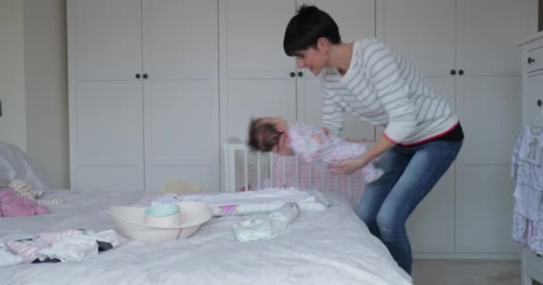 Baby has had her nappy changed by her mother on the double bed. The mother is fastening the baby grow while being playful. - Кадры, видео