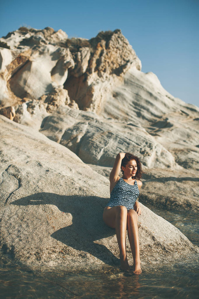 Pretty young woman on the stony seaside beach at summer day - Фото, зображення