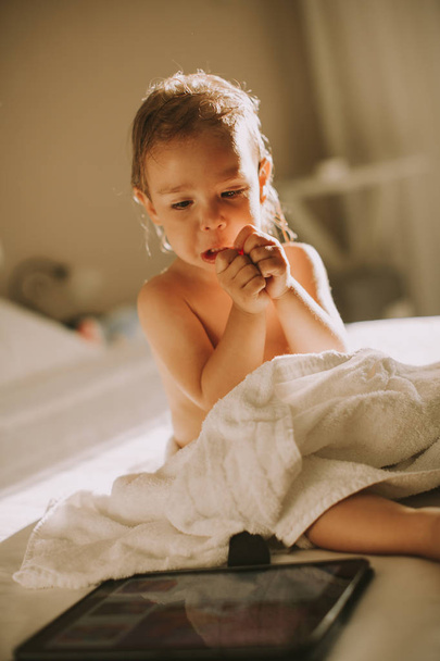 Doce menina encaracolado com uma toalha sobre seu corpo molhado situado em um quarto após o banho ou banho
 - Foto, Imagem