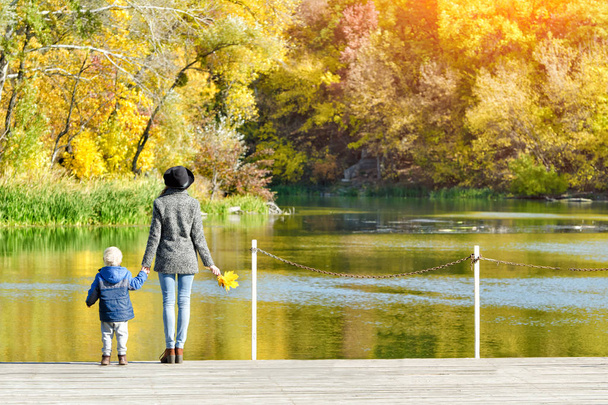 Mutter und Sohn stehen auf der Seebrücke am Fluss. Herbst, sonnig - Foto, Bild