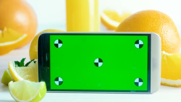 Primer plano 4k metraje de teléfono móvil con croma pantalla verde clave de pie en la mesa junto al vaso de jugo na frutas frescas. Perfecto para su anuncio de comida culinaria o saludable
 - Metraje, vídeo