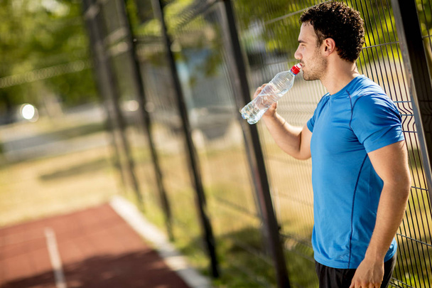 Handsome yung man drinking water from the bottle outdoors - Photo, Image