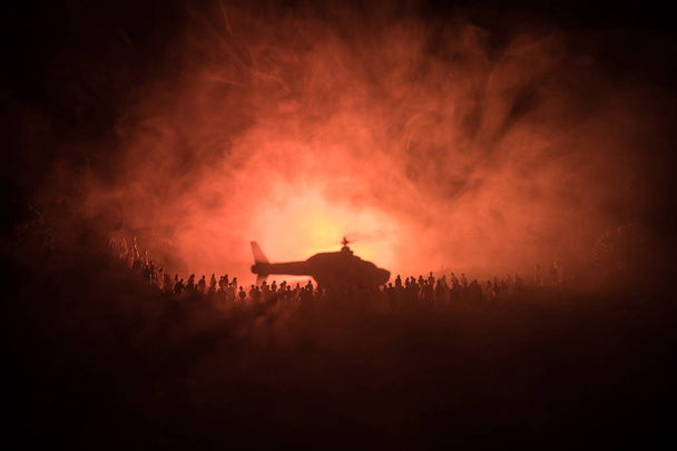 Военный вертолет готов к полету из зоны конфликта или силуэтов большой толпы людей, пытающихся сбежать с вертолетом. Украшенная ночь установлена фото
 - Фото, изображение
