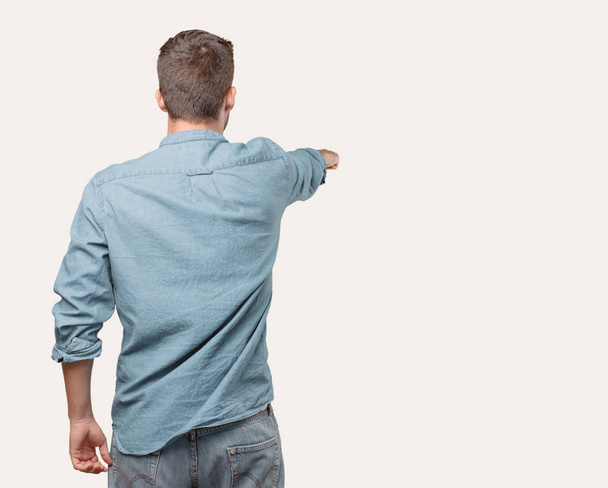 Young handsome man, blue denim shirt, back pose, pointing far. Person isolated against monochrome background. - Valokuva, kuva