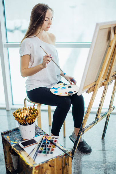Painter, european girl drawing sea-scape on canvas in her workshop. Concept of fine-art classes - Фото, изображение