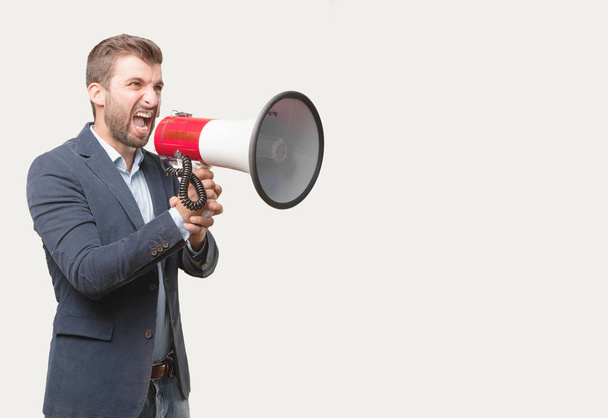 Young handsome businessman, blue blazer, shouting on a megaphone. Angry expression. Person isolated against monochrome background. - Foto, Bild