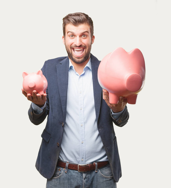 young handsome businessman, blue blazer, holding a piggy bank, happy or celebrating his success expression. Savings concept. Person isolated against monochrome background. - Foto, Imagen
