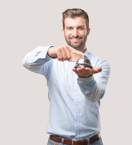 Young handsome man, blue t shirt holding a ring bell happy and smiling. Support expression. Person isolated against monochrome background. - Foto, imagen
