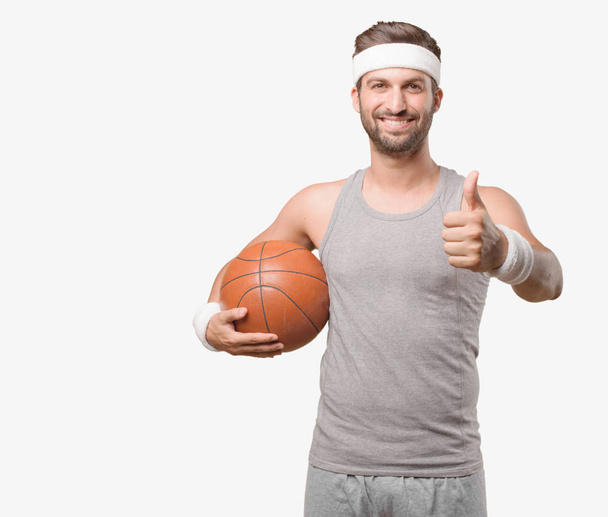 Young handsome sportsman with a basket ball and gray tank top. Person isolated against monochrome background. - Photo, Image