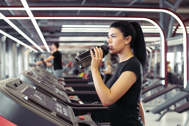 Young woman at treadmill drinking water - Фото, зображення