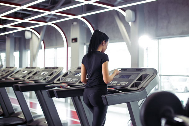 トレッドミルでジョギングしながらトレーニングアプリのためのスマートフォンを使用してスポーツ女性 - 写真・画像