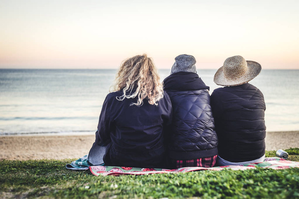 Three girls sitting on the blanket with the sea view - Zdjęcie, obraz
