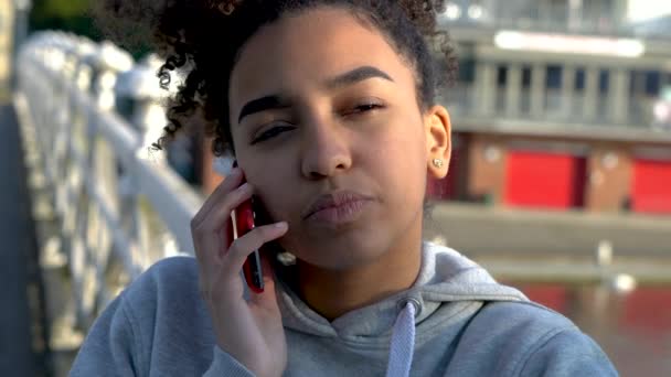 4K video clip of beautiful mixed race African American girl teenager young woman on a bridge over a river, talking on a mobile cell phone  - Video