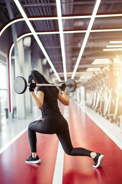girl doing lunges with barbell in modern gym - Foto, Imagem