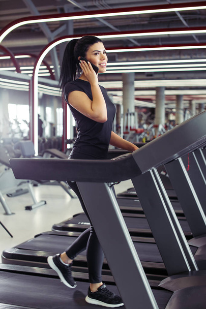 woman smiling while talking on mobile phone while running on treadmill - 写真・画像