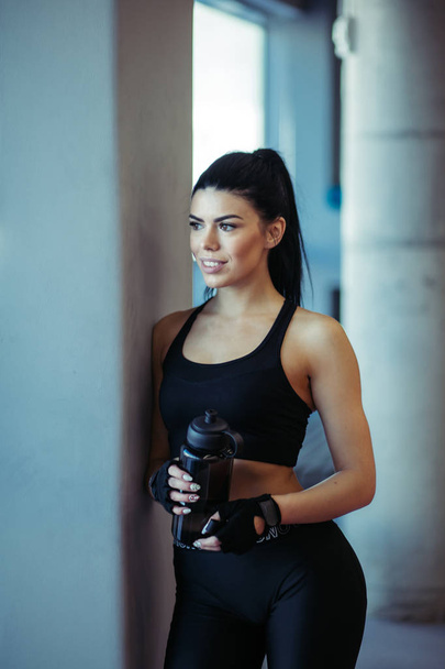 Female fit model posing with water after training near windows in gym - 写真・画像