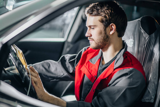 Mechanic Sitting In Car Looking At Digital Tablet in garage - Foto, imagen