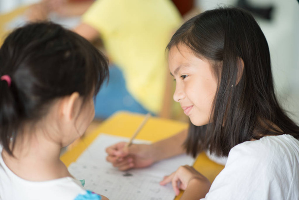 Pouco asiático menina escrevendo no notebook escola classe
 - Foto, Imagem