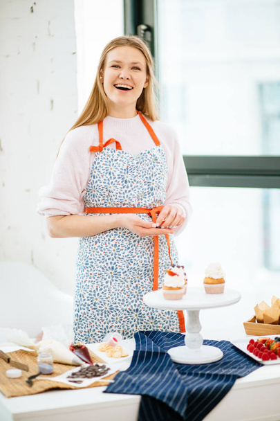 Pretty young woman decorating cupcakes on her kitchen - Φωτογραφία, εικόνα