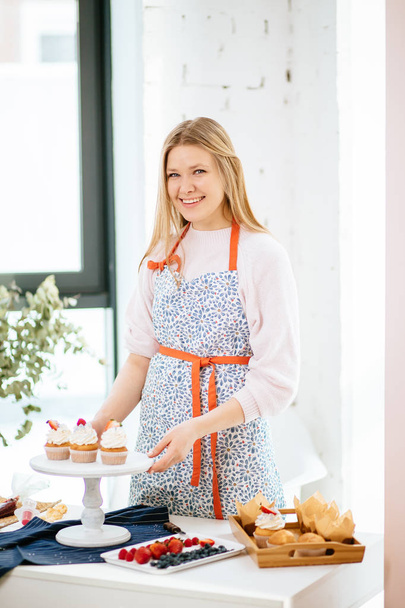 Happy young pastry woman demonstrating freshly baked cupcakes looking at the camera and smiling - Φωτογραφία, εικόνα