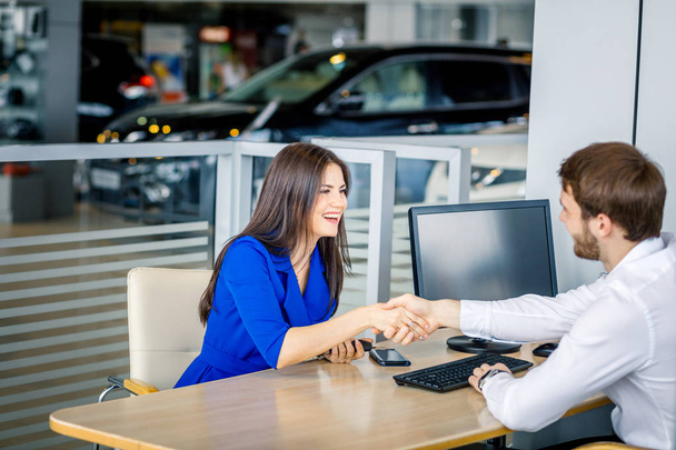 Sales manager and female customer shaking hands congratulating each other at the dealership showroom. - Photo, Image