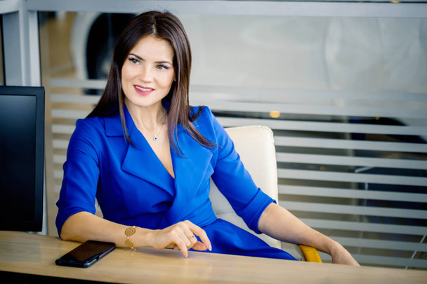 Mulher de negócios bonita em azul sentado à mesa
 - Foto, Imagem