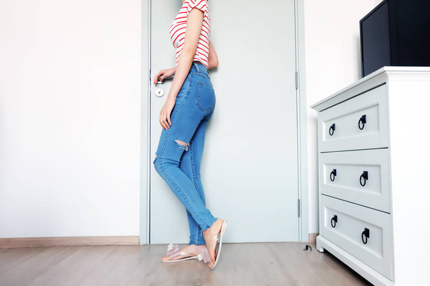 Summer Fashion Nude Bow Sandal (Footwear) and Slim Legs in The Room. Female Sexy Long Legs. Beautiful Slim Legs Woman Standing with Nude Sandals and Lack Blue Jean on Wooden Floor at Home Background - Фото, изображение