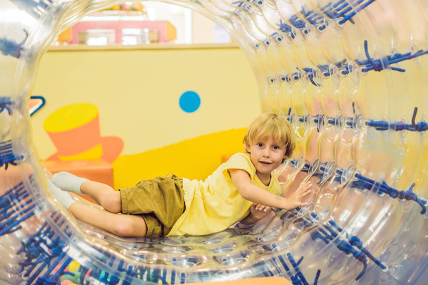 Cute little boy, playing in Zorb a rolling plastic cylinder ring with a hole in the middle, intdoor. - Foto, immagini