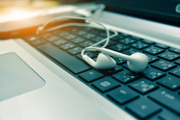 人々 は娯楽のため白のイヤホンを使用してインターネット上の音楽に耳を傾けます。人々 は、インターネットを介してオンライン ショッピングが、白いヘッドフォンがコンピューターのキーボード上に配置 - 写真・画像