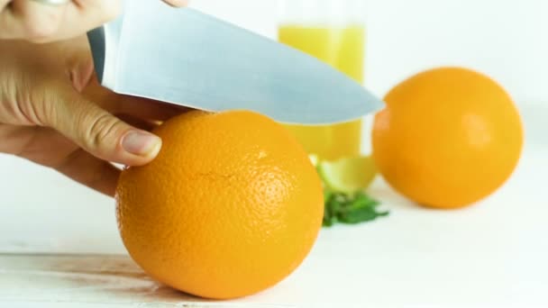 Closeup slow-motion beelden van vrouw snijden oranje in twee helften met grote mes op witte houten tafel - Video