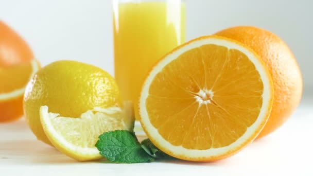 Zbliżenie slow motion video panoramowanie kamery wzdłuż asortyment owoców cytrusowych i szklankę soku pomarańczowego na biały drewniany stół - Materiał filmowy, wideo
