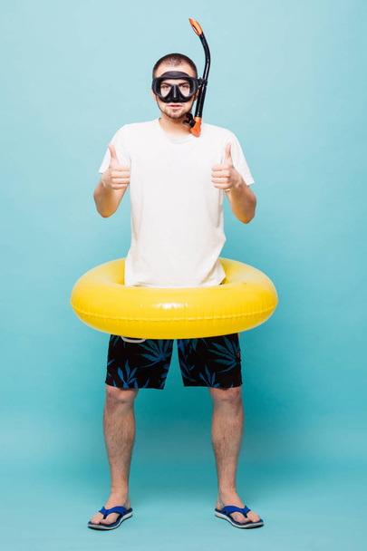 Longitud completa Joven hombre guapo con anillo amarillo inflable y snorkel con pulgares hacia arriba aislado sobre fondo verde
 - Foto, Imagen