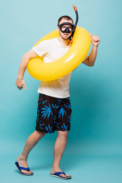 voller Länge junger gutaussehender Mann mit aufblasbarem gelben Ring und Schnorchelmaske, der isoliert auf grünem Hintergrund davonläuft - Foto, Bild