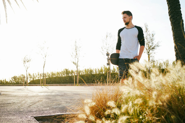 Νεαρός άνδρας στο casual ρούχα που στέκεται σε μια ζώνη skate με skateboard  - Φωτογραφία, εικόνα