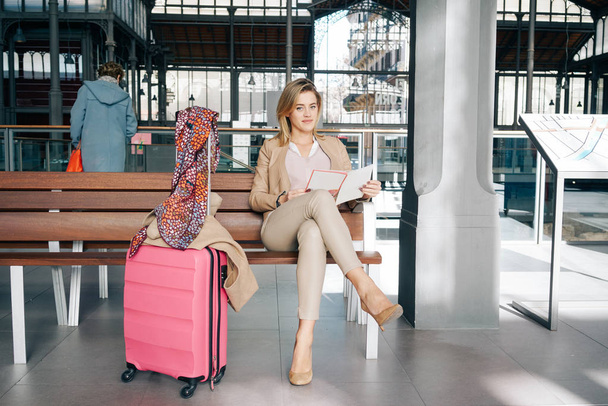 Beautiful young woman using laptop while sitting with luggage in train station - Foto, imagen