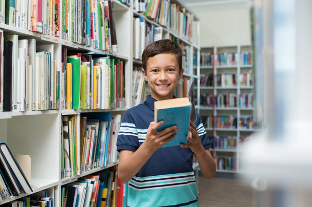 Boy holding book in library at school - Foto, imagen