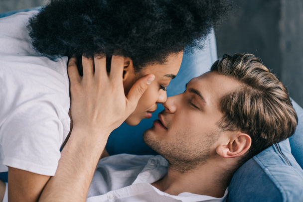 Jeune couple multiracial embrasser tout allongé sur le canapé
 - Photo, image