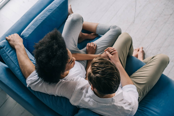 Multiracial couple holding hands while sitting on sofa - Fotoğraf, Görsel