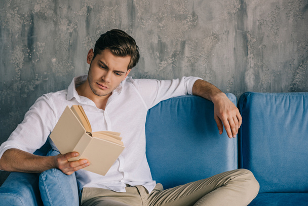 Thoughtful man reading book while sitting on sofa - Foto, Bild