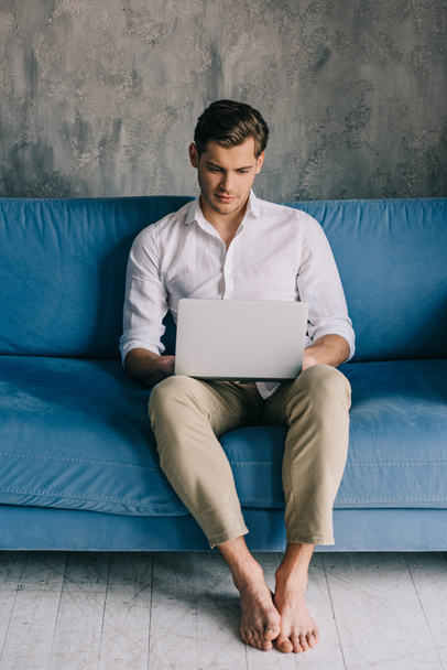 Young man working on laptop while sitting on sofa - Foto, Imagem