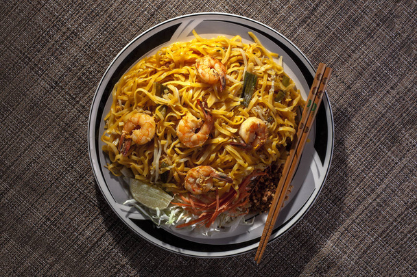 Delicious stir fried noodles called pad thai in thailand is a tasty dish.  It is made with seafood such as shrimp or prawn and pasta. The image shows lunch with chopsticks - Foto, Bild