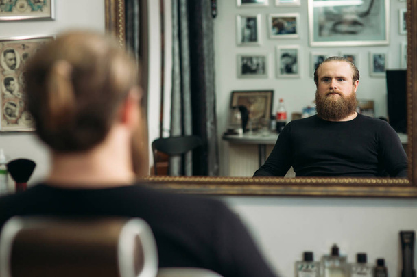 handsome young bearded guy sitting in an armchair in a beauty salon - Photo, Image