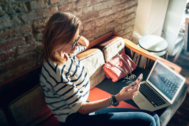 jovem bela empresária escreve uma mensagem no smartphone durante a pausa para o almoço enquanto se senta à mesa com laptop
 - Foto, Imagem