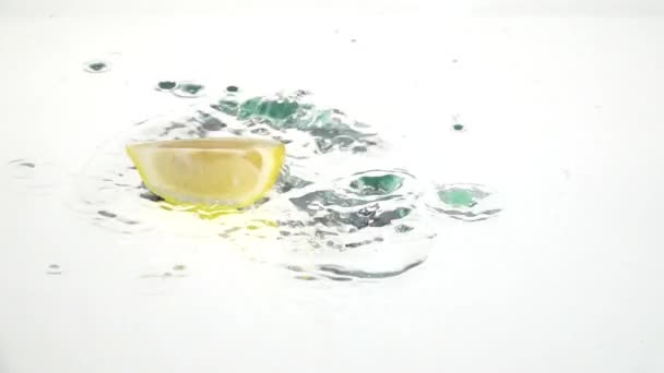 Quarter of a lemon drops into the water and remains there. White background. Slow motion - Záběry, video