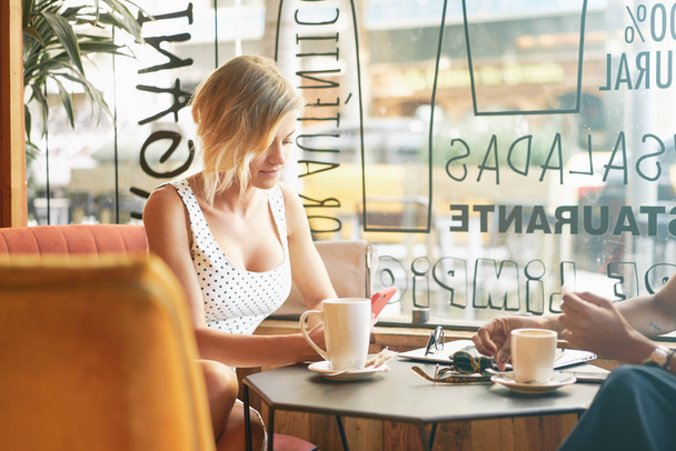 Two young women talking while having coffee break in a cafe with modern interior - Фото, зображення