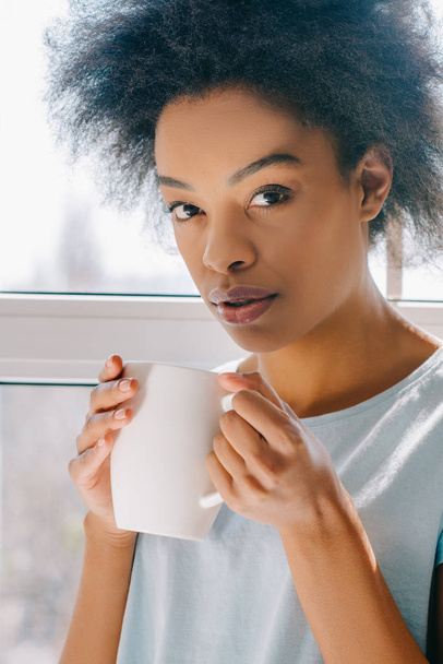 African american girl in lounge wear drinking coffee from cup - Zdjęcie, obraz